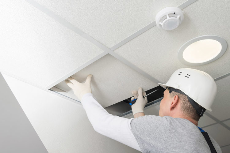 man in hardhat removing a hanging ceiling tile