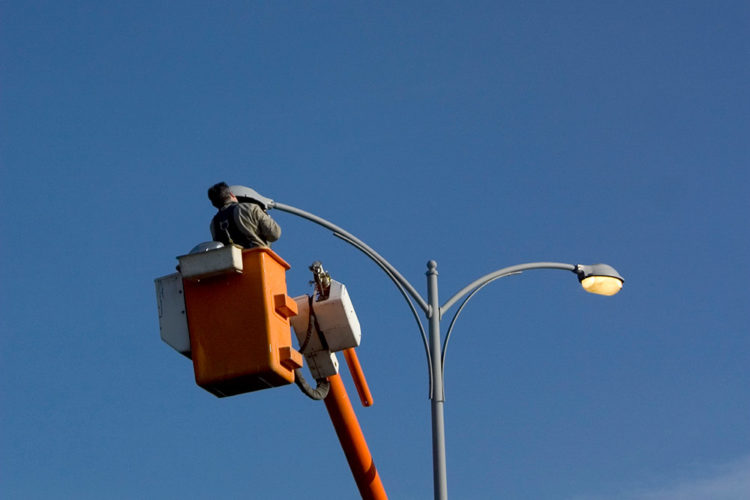 man in hi-lift bucket replacing light bulb in parking lot light post